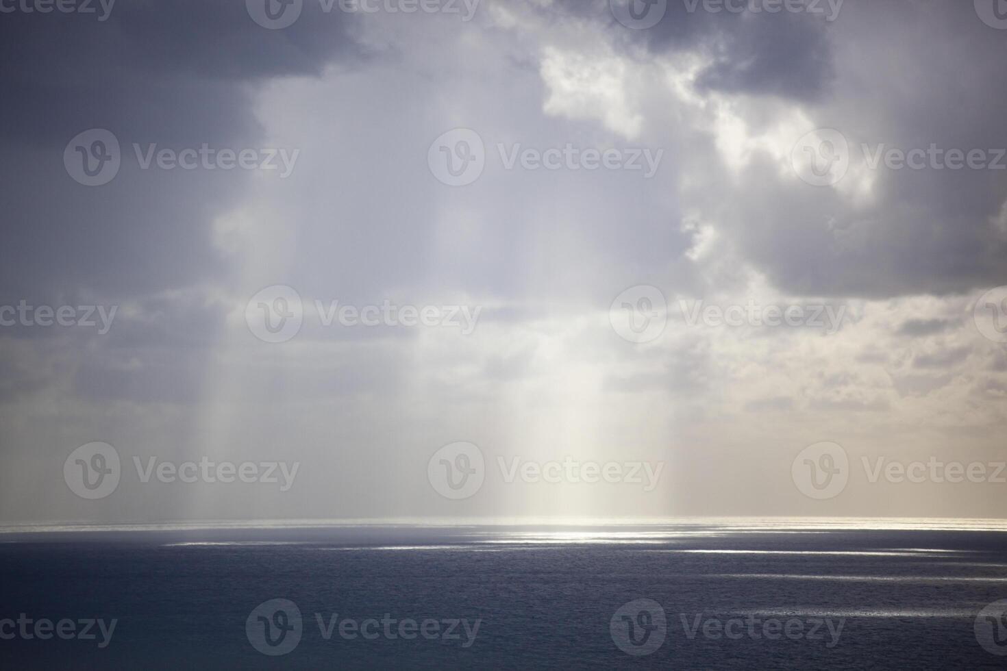 Overcast grey sky with low textured clouds. Sunlight peeks through the clouds and falls on the sea. Background. Horizontal photo