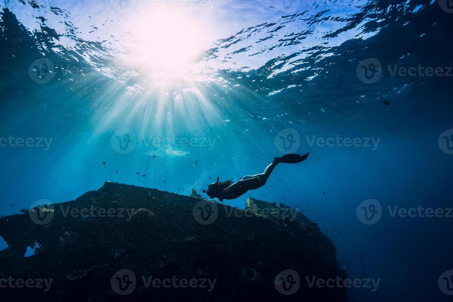 Free diver girl in pink swimwear with fins swimming underwater at wreck ship. Freediving in the ocean photo