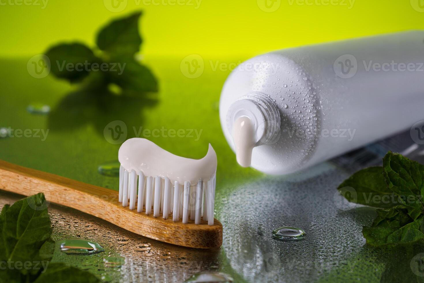 Close up tube of toothpaste and bamboo toothbrush on wet reflective surface with fresh mint leaves. Oral care featuring.Concept oral health and care. International Dentist Day. National Brush Day photo