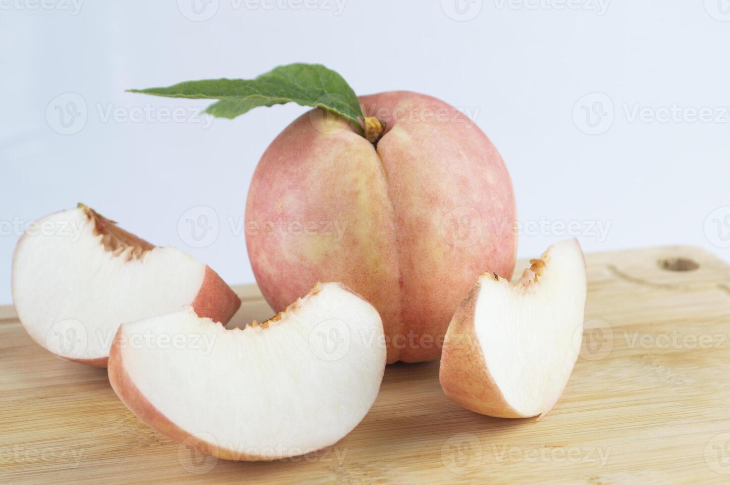a peach with a slice cut in half and a green leaf photo