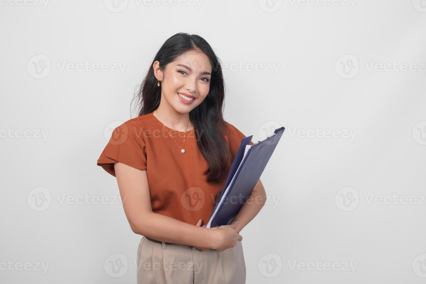 Beautiful young Asian woman wearing brown shirt smiling while holding document over isolated white background. photo