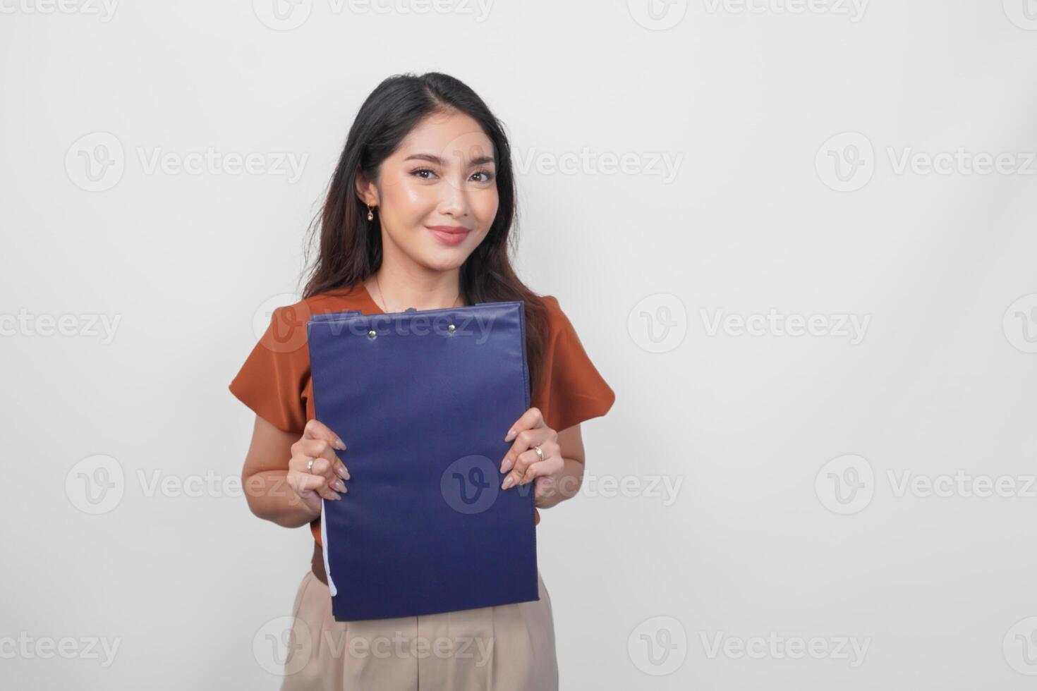 Happy young Asian woman wearing brown shirt smiling while holding and showing document over isolated white background. photo