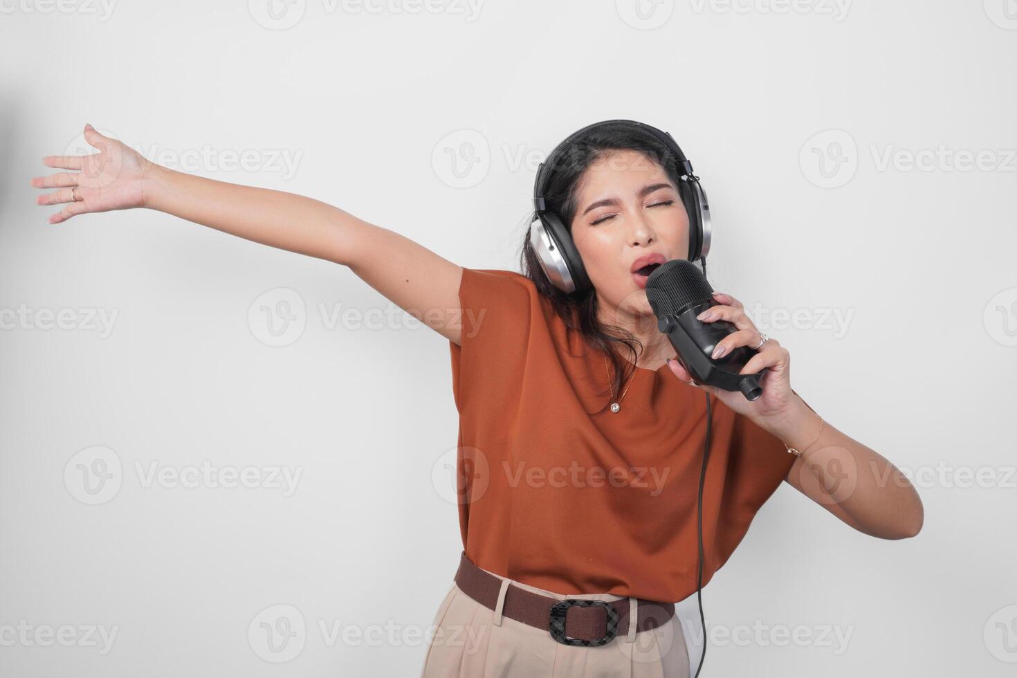 Overjoyed young woman wearing brown shirt and headphone to listen music and singing along isolated over white background. photo