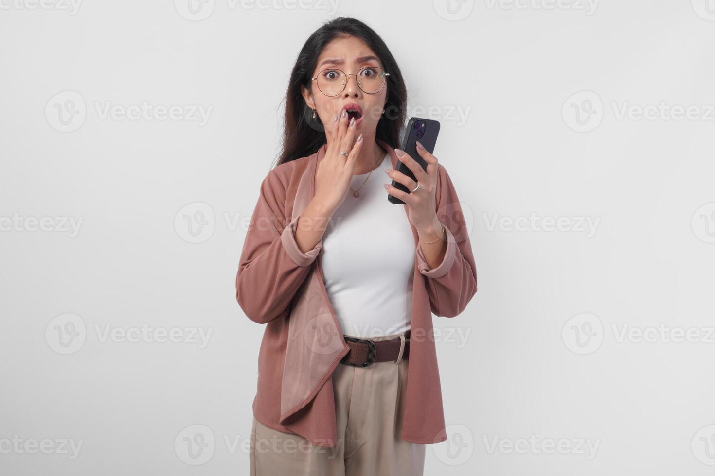 Shocked Asian business woman in eyeglasses pointing to her smartphone, isolated by white background. photo