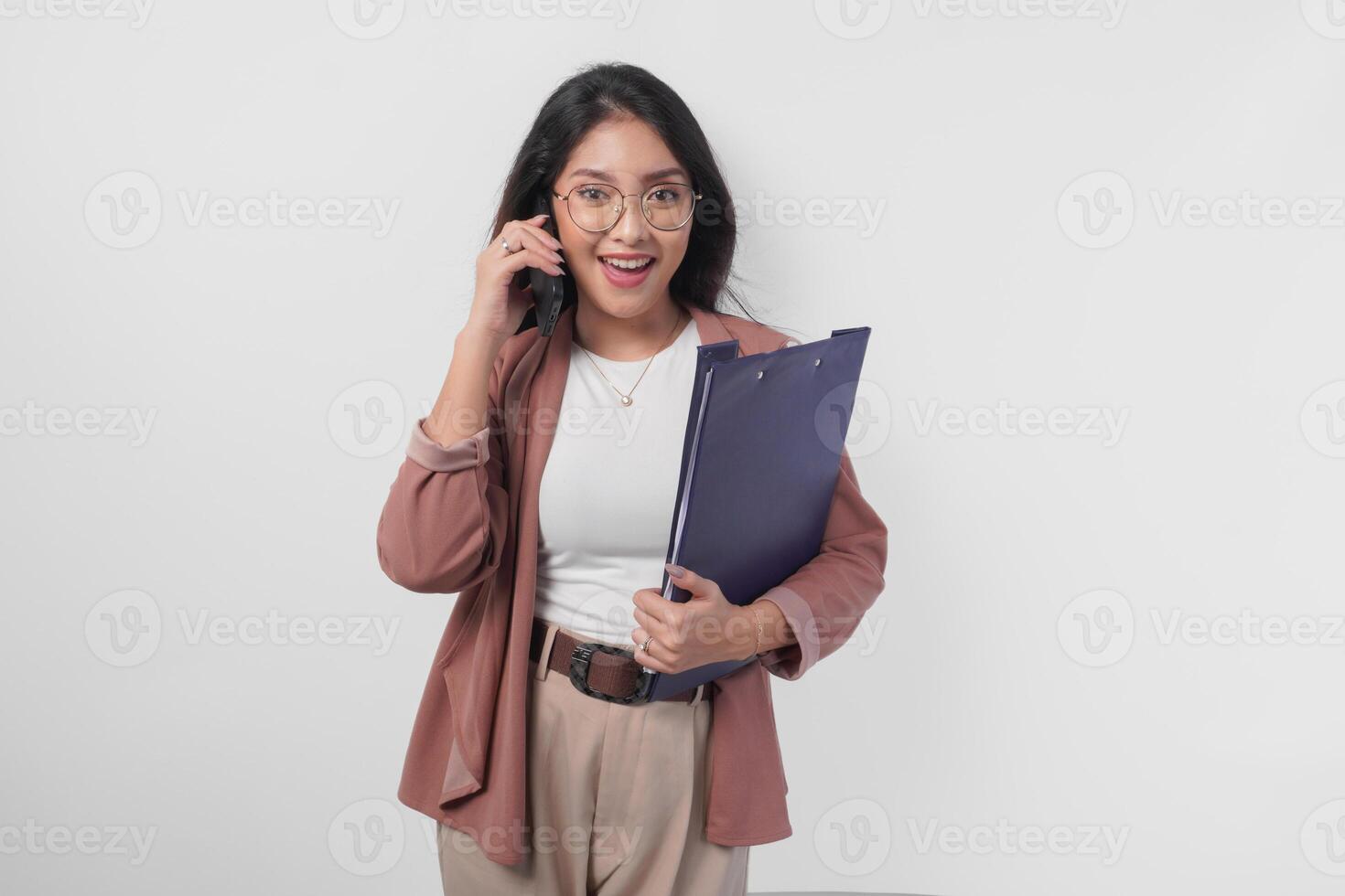 Smiling Asian business woman in eyeglasses holding a document while having a call for meeting, isolated by white background. photo
