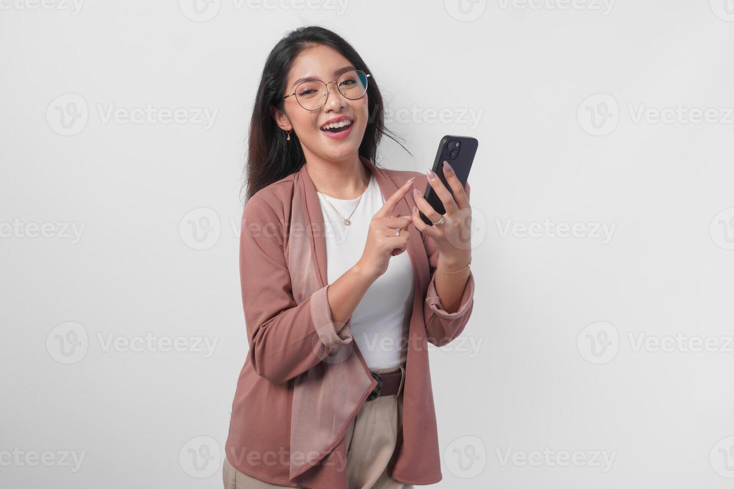 Smiling Asian woman in eyeglasses using phone to text or browse internet, isolated by white background. photo