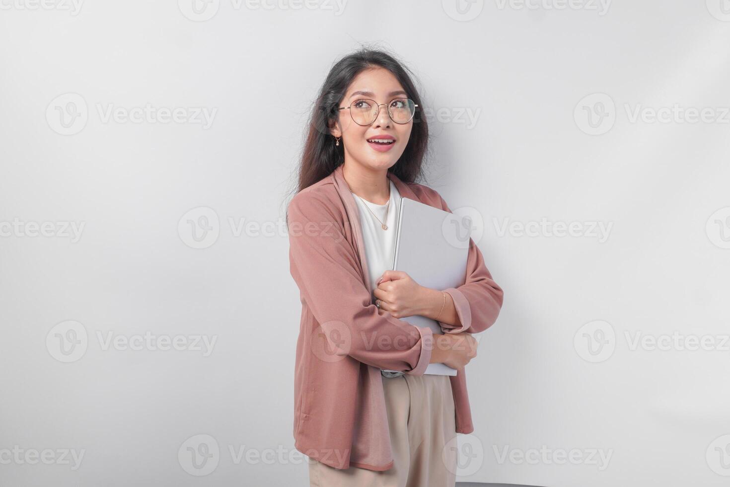 Attractive young Asian business woman holding a laptop close while smiling happily over isolated white background. photo