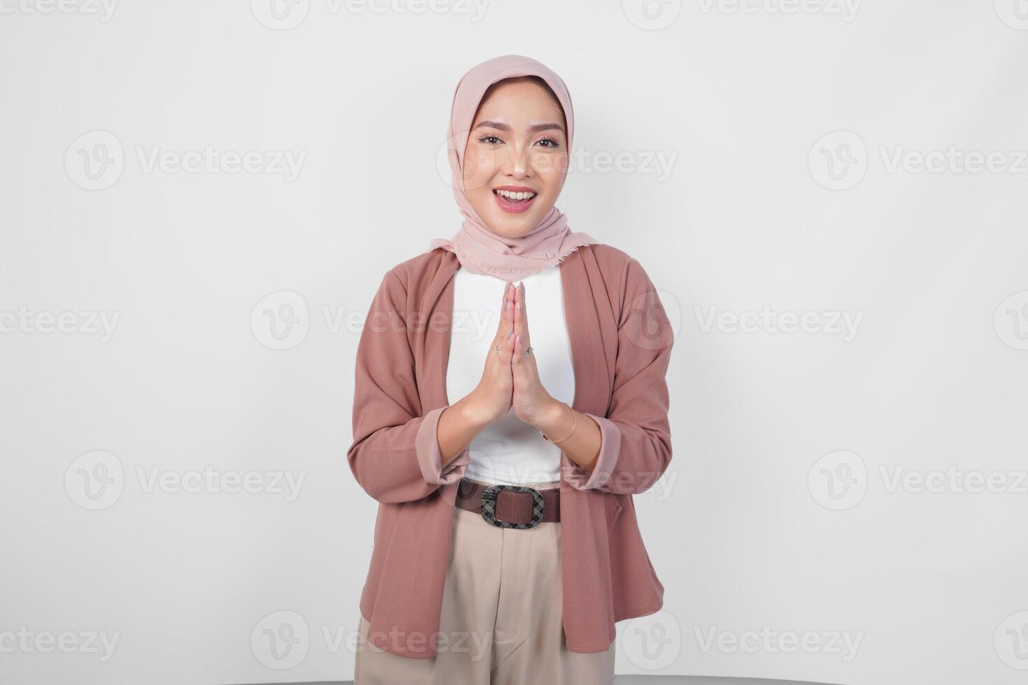 Elegant Asian Muslim woman wearing veil hijab smiling to the camera and gesturing traditional greeting isolated over white background. photo