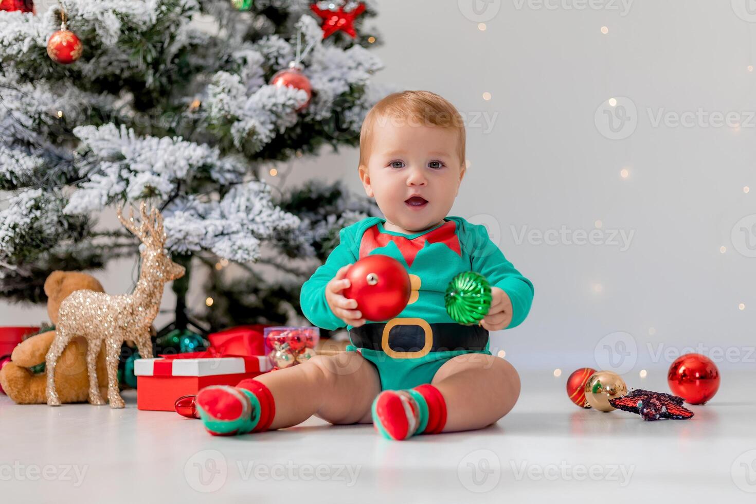 baby in green bodysuit holds colorful Christmas balls in his hands. kid in a Christmas gnome costume photo