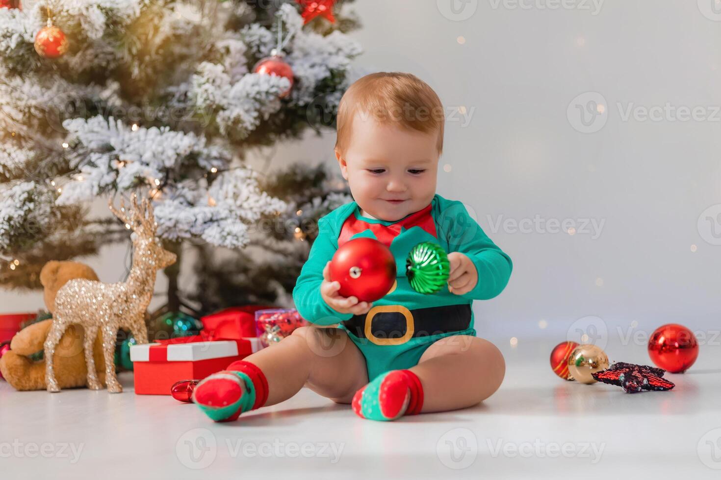 baby in green bodysuit holds colorful Christmas balls in his hands. kid in a Christmas gnome costume photo