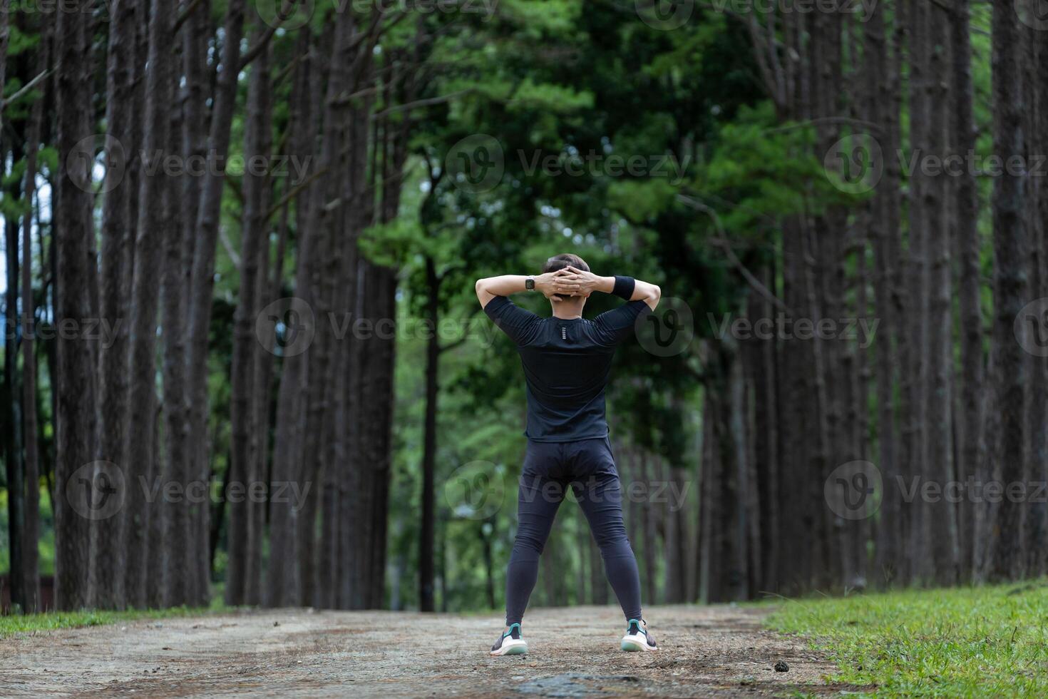 Trail runner in black clothe is stretching for warm up outdoor in the pine forest dirt road for exercise and workout activities training for achieving healthy lifestyle and fitness photo