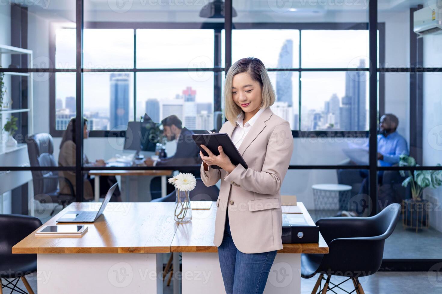 Portrait of Asian business CEO woman is standing in office at the table with digital tablet and showing statistic chart showing annual report and skyscraper background photo