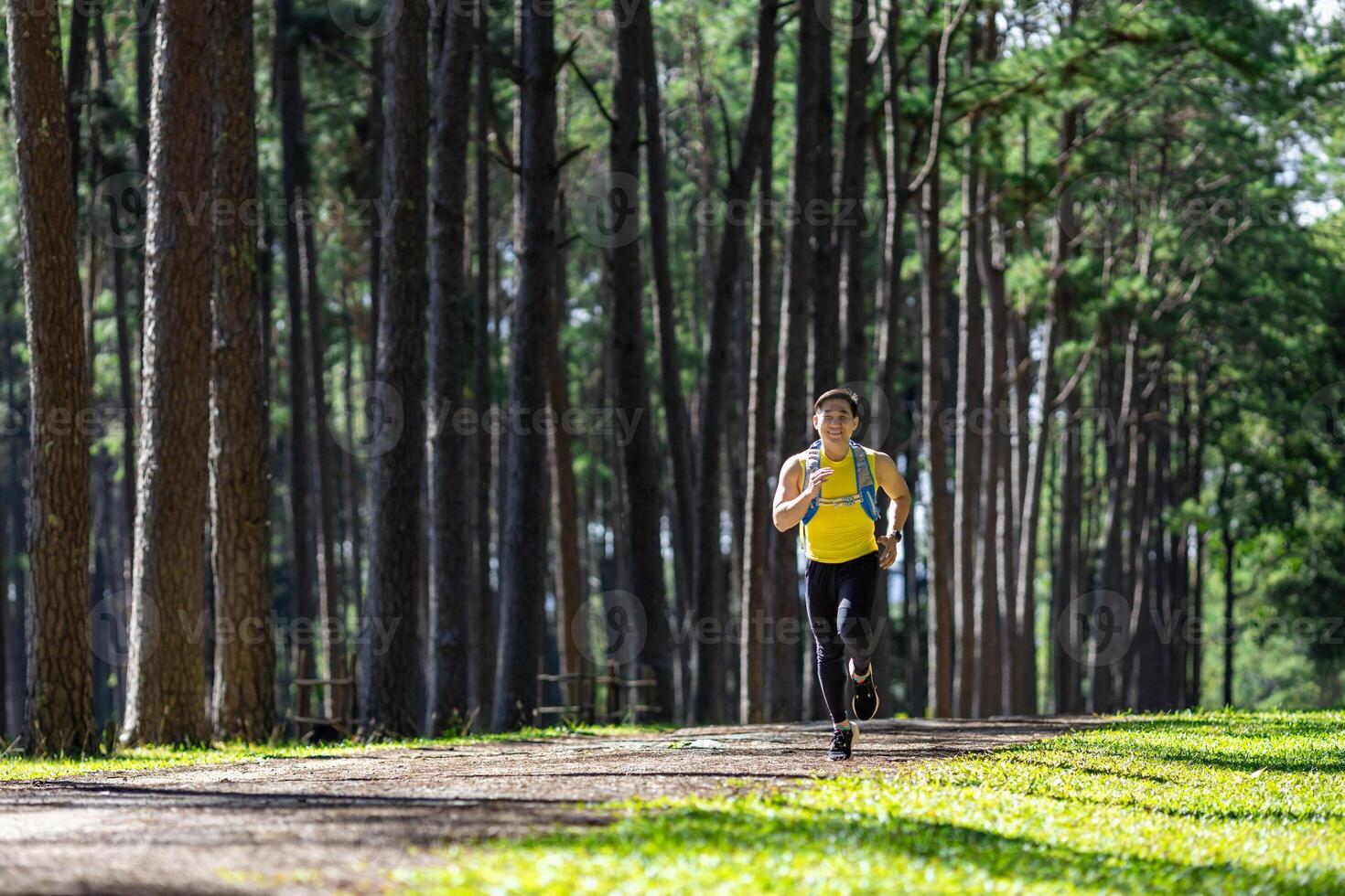 Asian trail runner is running outdoor in the pine forest dirt road with water backpack for exercise activities training to race in the ultra marathon to achieve healthy lifestyle and fitness photo