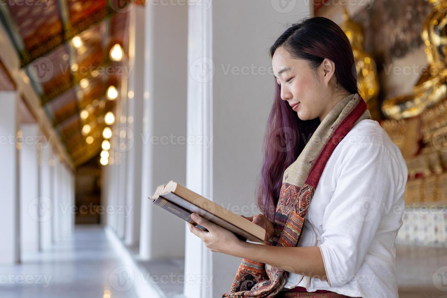 Asian buddhist woman is reading Sanskrit ancient Tripitaka book of Lord Buddha dhamma teaching while sitting in temple to chant and worship inside the monastery photo