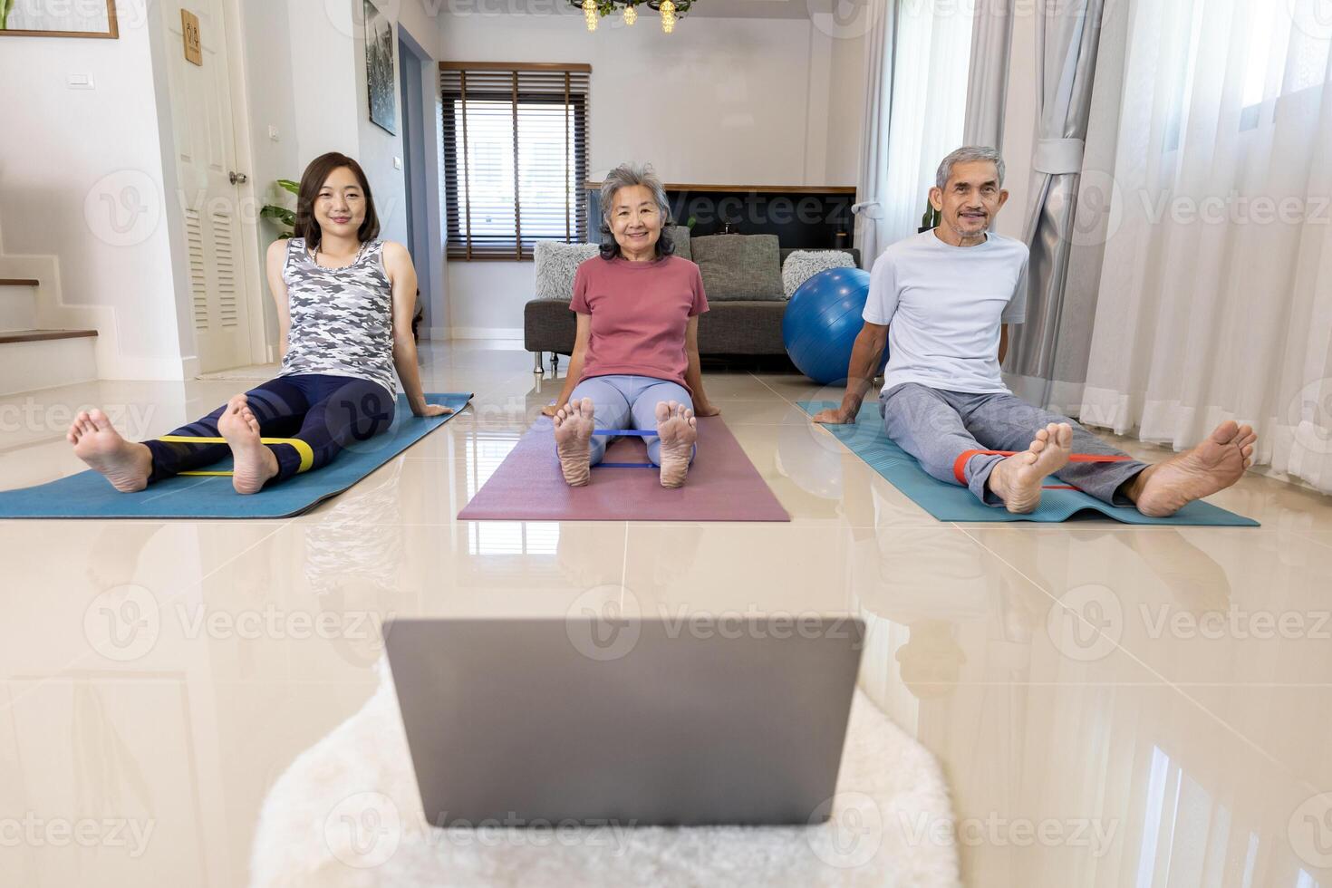 Senior asian couple and daughter are exercising at home doing elastic resistance rubber band with online trainer class from internet for elder healthy and longevity photo