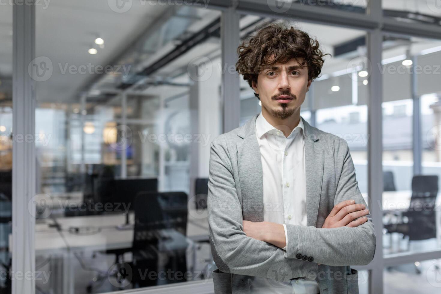 Portrait of hispanic businessman inside modern office, boss serious looking at camera, man with crossed arms thinking worker. photo