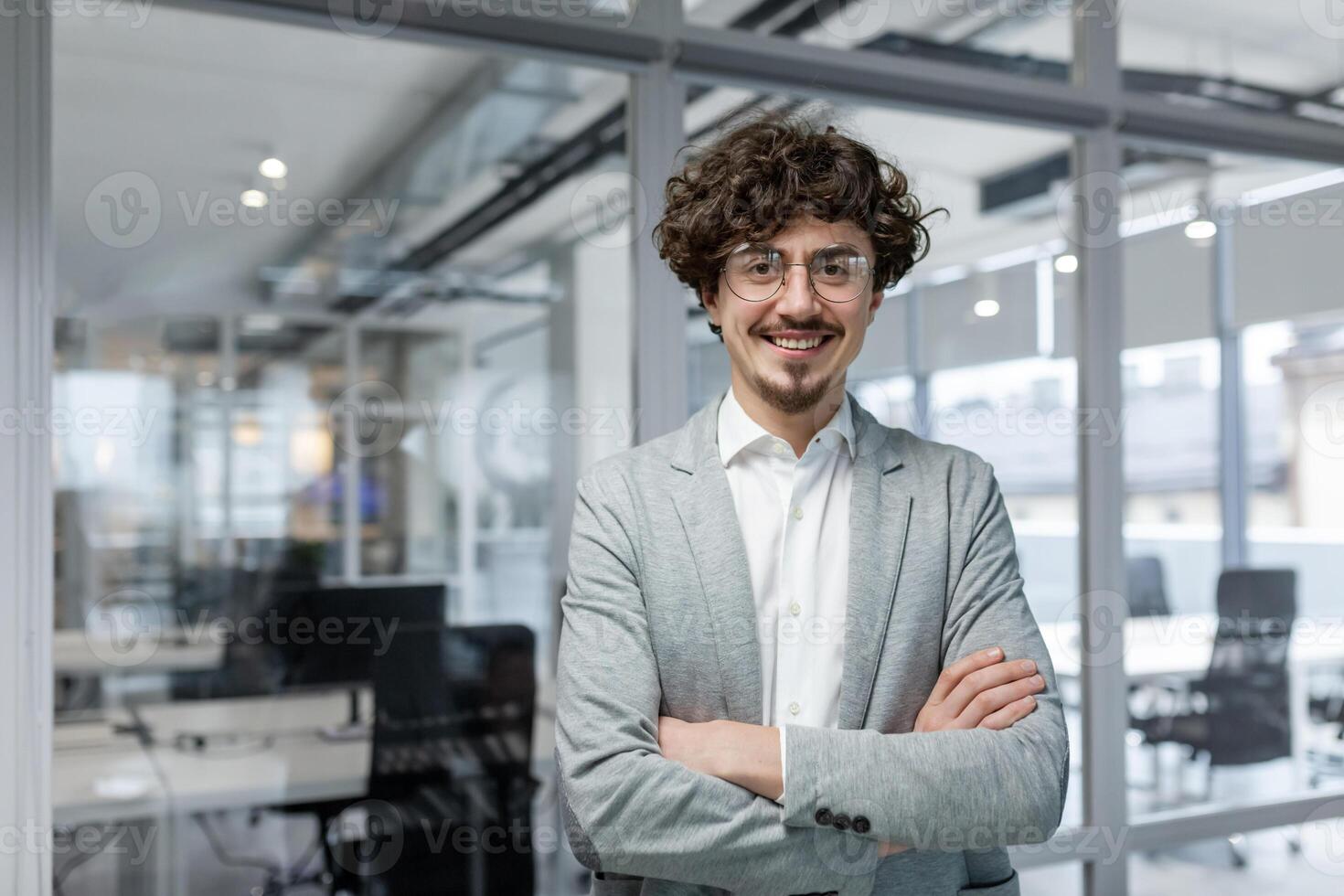Portrait of successful mature boss, senior businessman in glasses and business suit looking at camera and smiling, man with crossed arms working inside modern office building photo