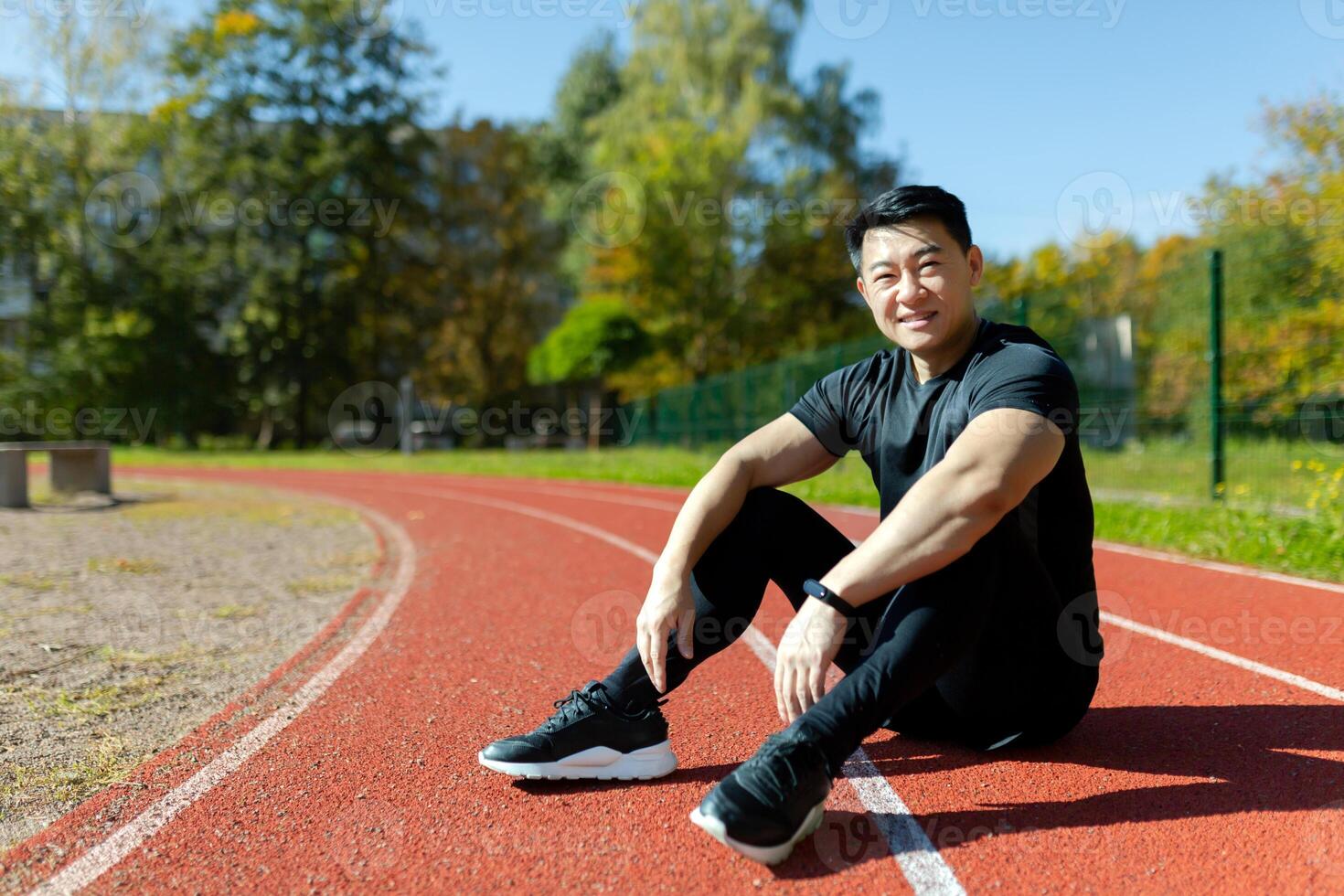 Young asian sportsman, spotter, runner sitting in stadium on treadmill and resting after jogging, exercise. Tired but smiling, he looks at the camera. photo