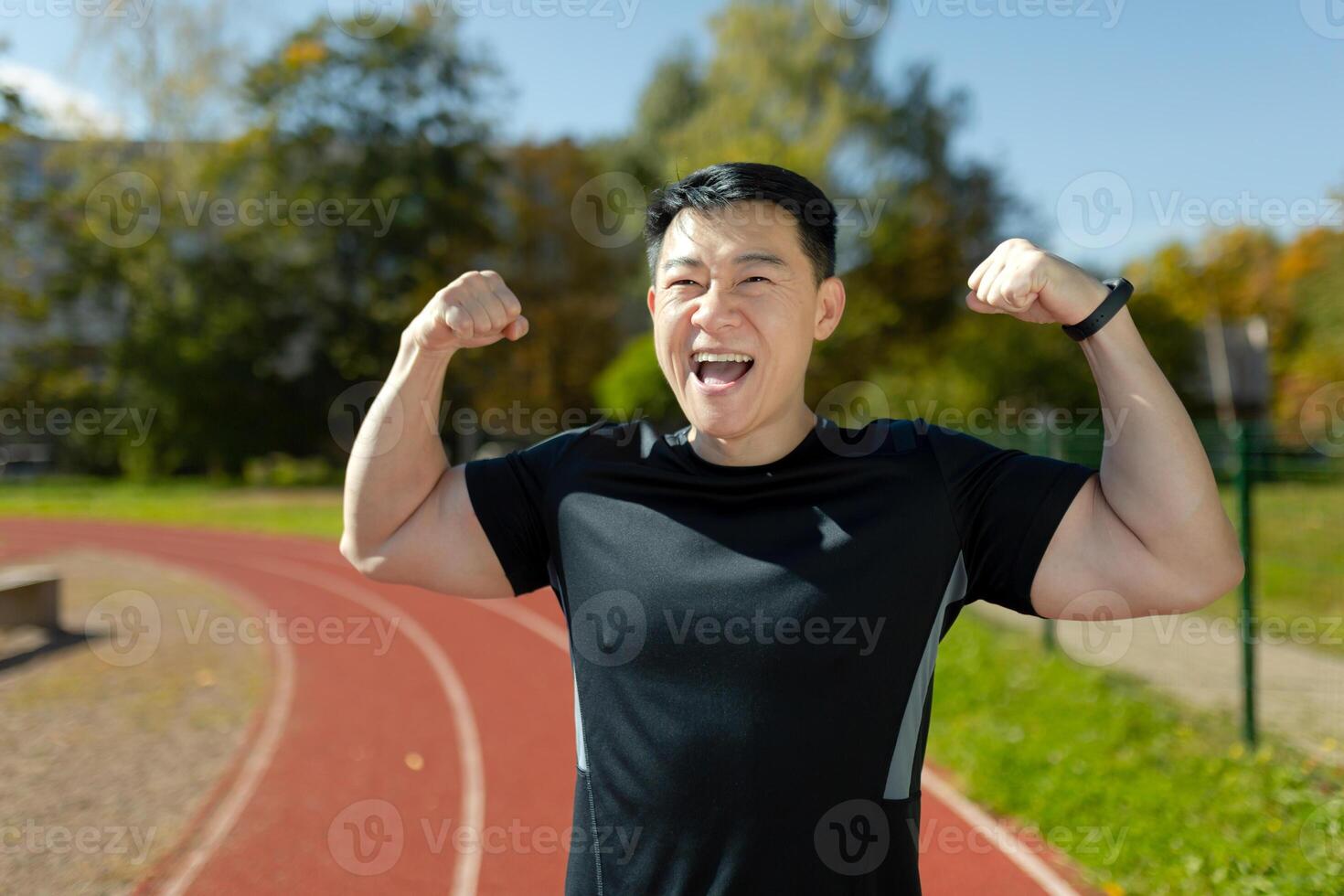 Winning the competition. A young Asian man, an athlete, a runner celebrates a victory in a race. Happy man standing in stadium on running track and showing strength and victory gestures with his hands. photo