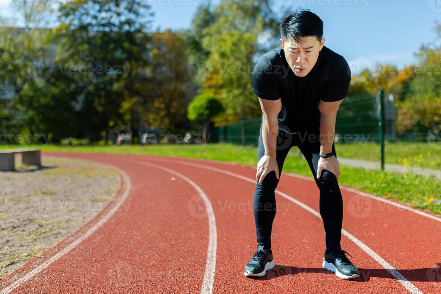 Asian sportsman tired after running and active physical exercise, man taking breath and rest on sunny day in stadium, overtired after running. photo