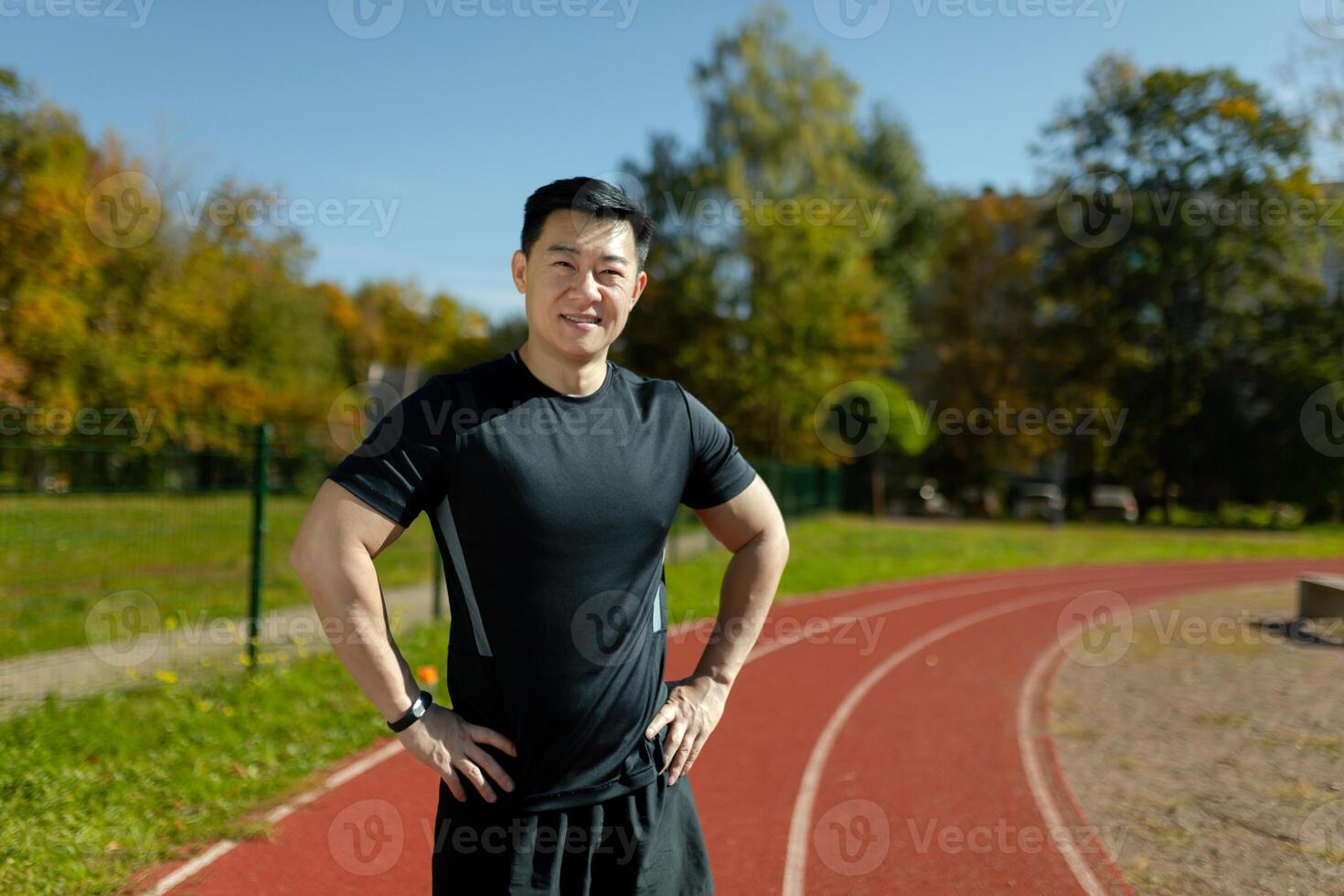 Portrait of a smiling and confident Asian male athlete standing in front of the camera in a stadium with his arms at his sides. photo