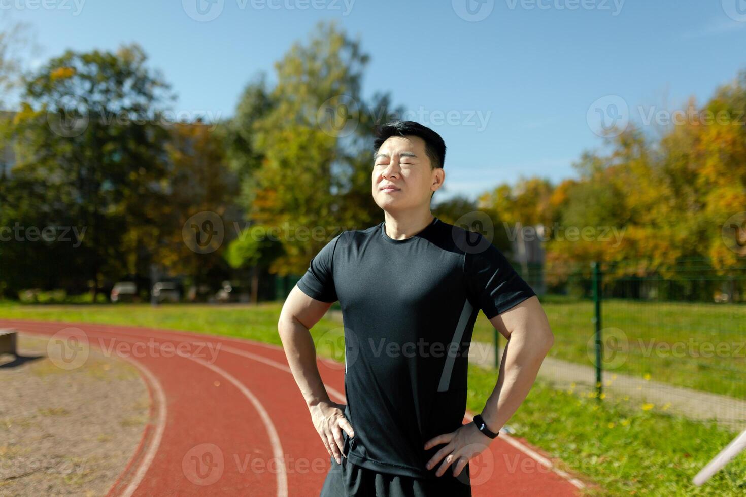 Portrait of a young Asian male athlete, trainer standing on a stadium treadmill. He closes his eyes, rests, breathes. Preparing for exercises, running. photo