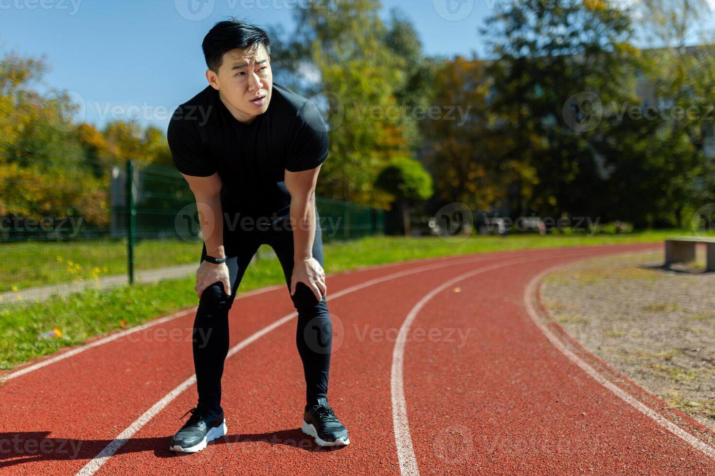 Asian sportsman tired after running and active physical exercise, man taking breath and rest on sunny day in stadium, overtired after running. photo