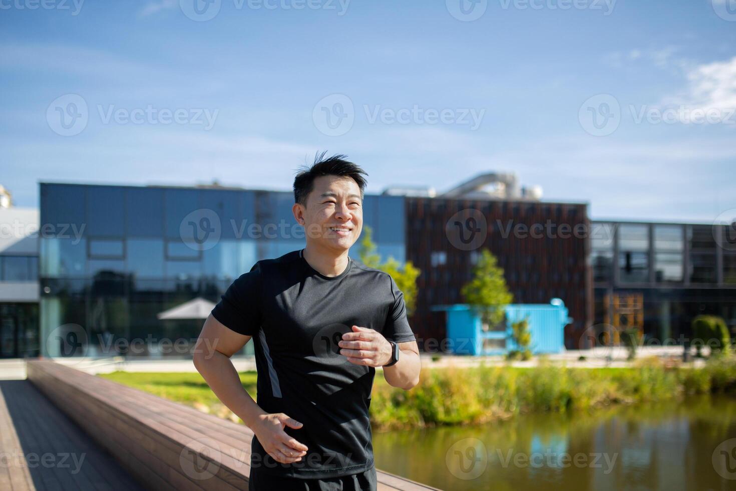Asian smiling young man dressed in sportswear is doing a morning jog in the park near the lake. photo