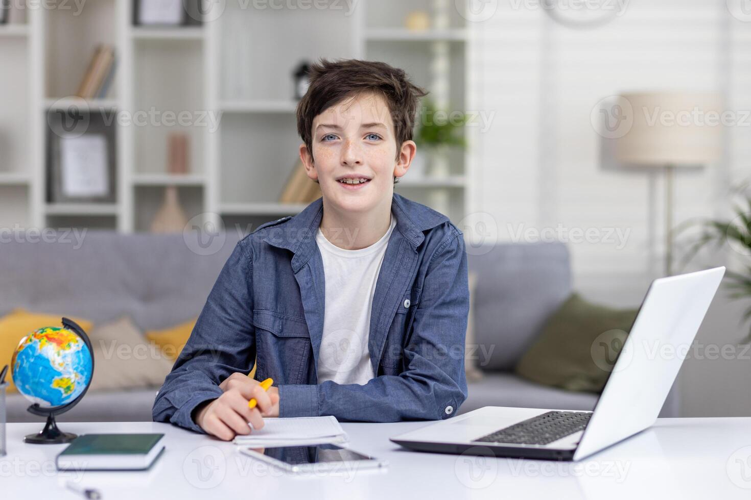 Portrait of happy teenage boy student sitting at table at home, studying via distance learning, doing homework, smiling, looking at camera. photo