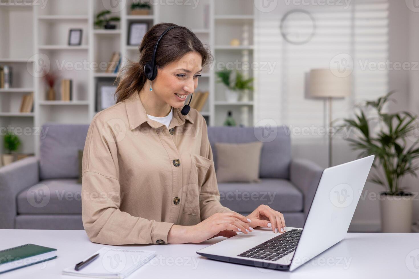 A young woman in a headset works in a call center, advises clients, a businesswoman works from home at a laptop, communicates on a call, smiles at the screen. photo