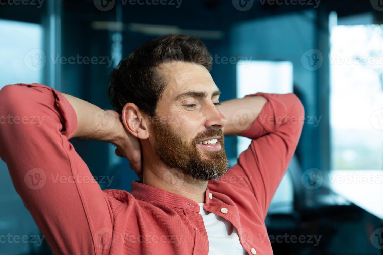 A young male programmer, a freelancer, is resting from a hard day in the office at his desk. He sits on a chair, closes his eyes, puts his hands behind his head, meditates, dreams, smiles. photo