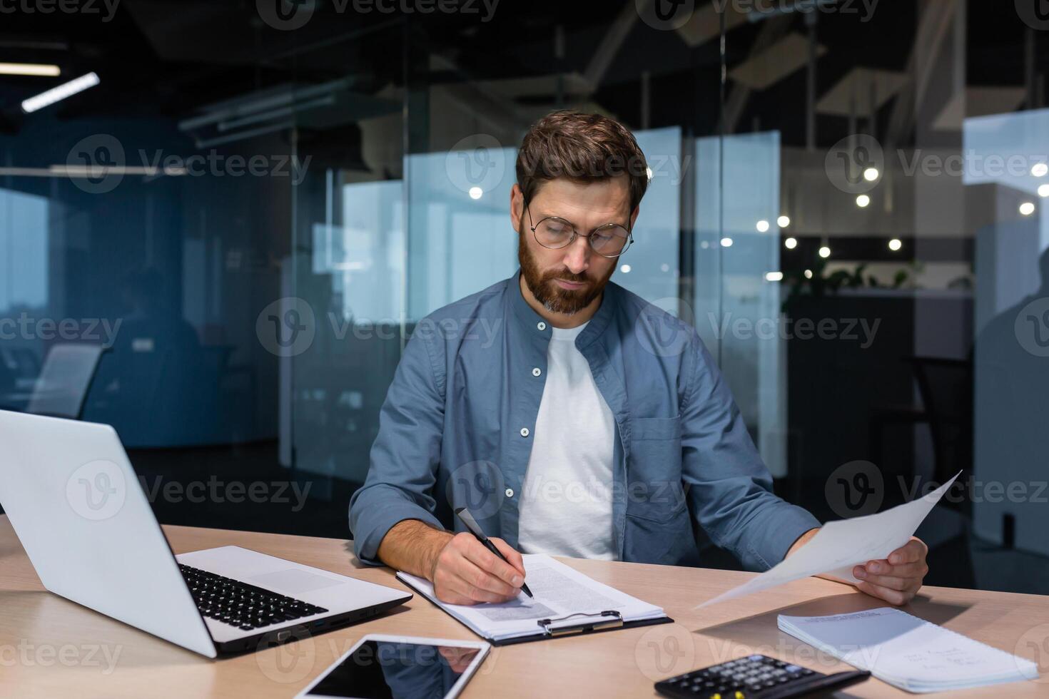 A serious young man accountant, financier, analyst, auditor sits in the office at the table. Works with documents. writes and calculates the budget, finances. photo