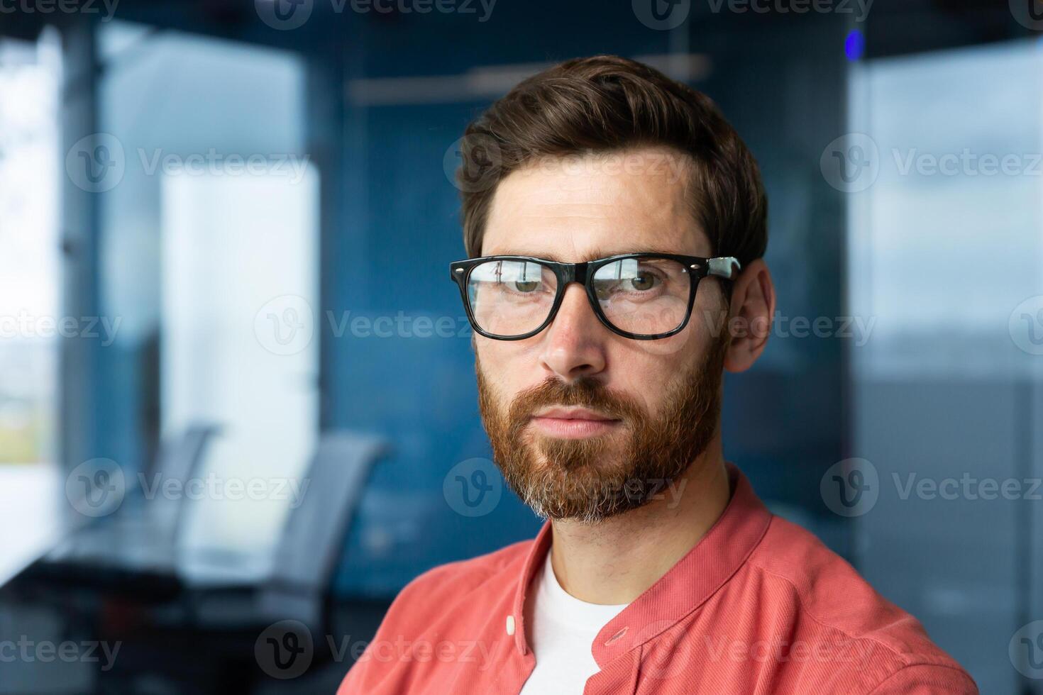 Close-up photo. Portrait of a young professional man, a developer in glasses and a red shirt who looks confidently into the camera. photo