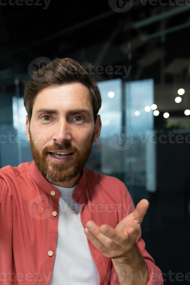 Close-up photo. Young businessman, freelancer, programmer conducts a conference on a call, holds a phone in his hands, talks to the camera, vertical photo. photo