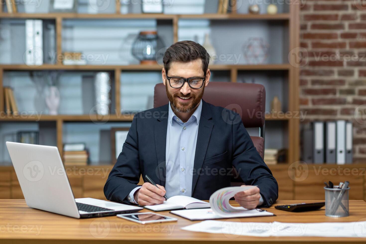 Mature businessman doing paperwork, man working with documents, contracts and bills sitting at table using laptop at work, financier accountant with beard and glasses. photo
