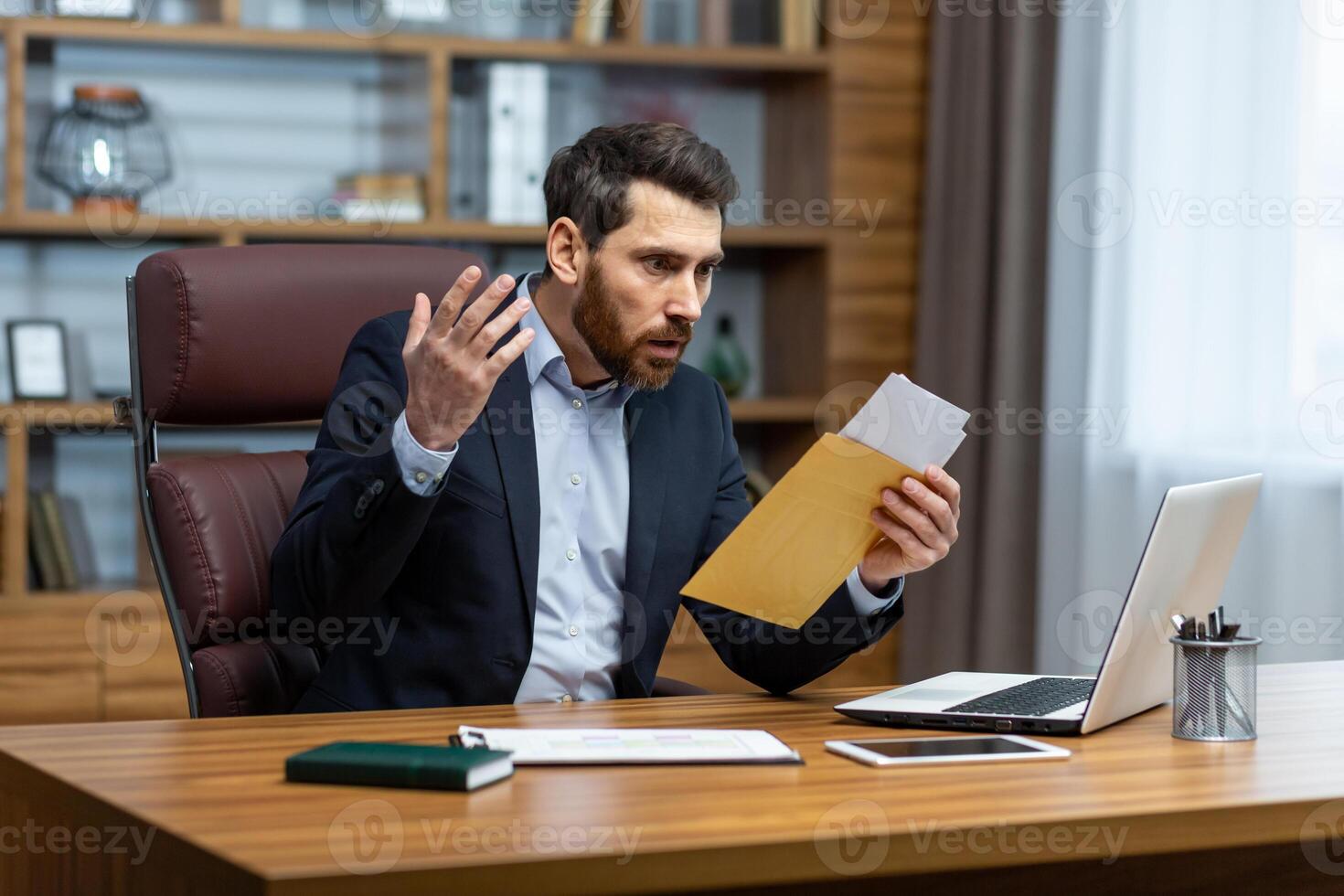 Upset and angry boss received mail message notification with bad news, male businessman working inside office with documents and papers, using laptop at work. photo