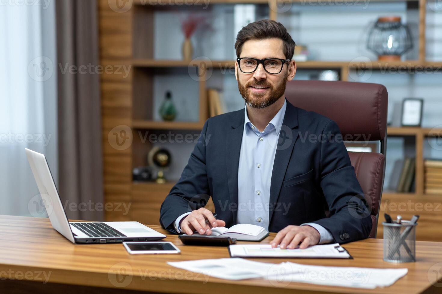 Portrait of successful businessman behind paper work, man in shirt smiling and looking at camera, financier boss inside office using laptop in work at workplace. photo