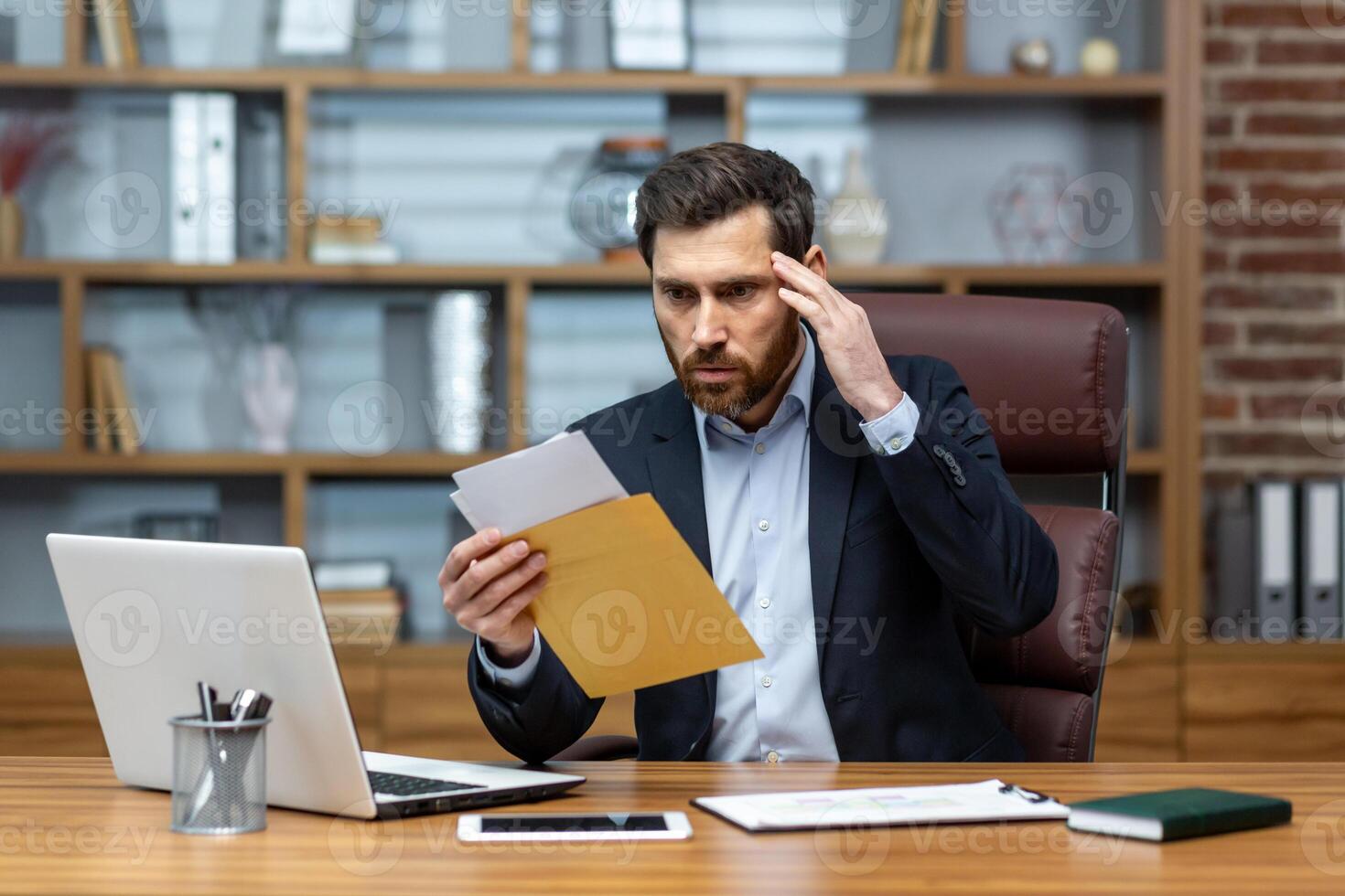 Upset and angry boss received mail message notification with bad news, male businessman working inside office with documents and papers, using laptop at work. photo