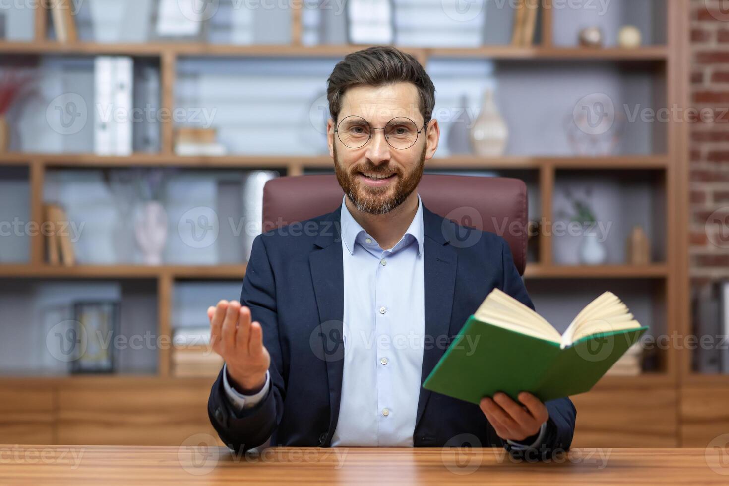 call online learning, teacher smiling and looking at web camera, man in suit giving lecture online sitting at table, holding book and smiling. photo