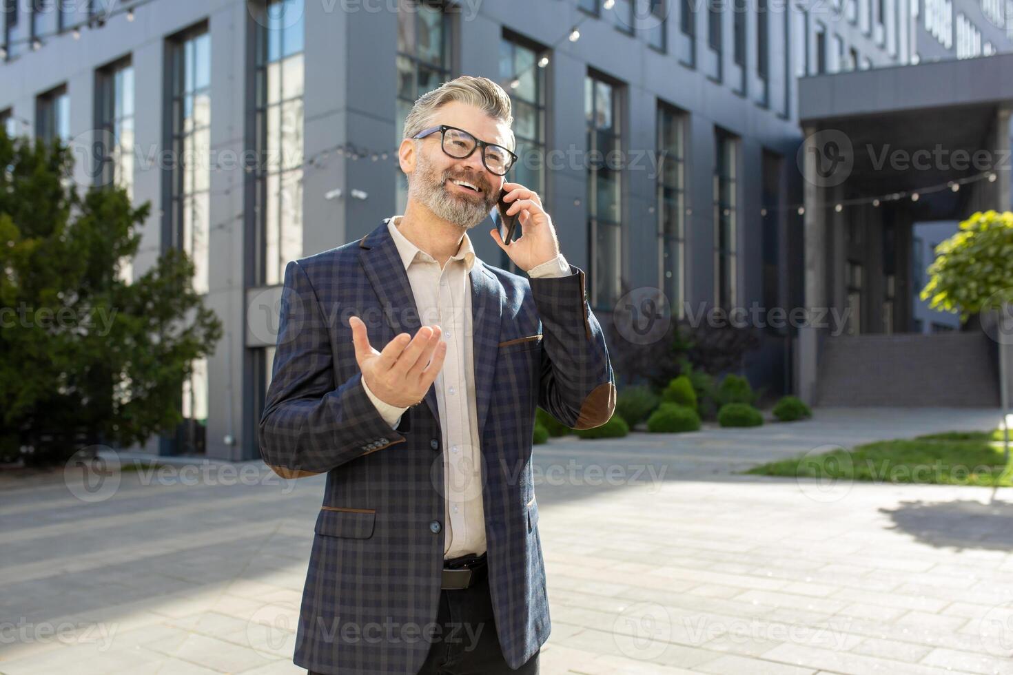 Mature businessman in stylish suit having a lively conversation on his mobile phone in front of an office building. photo