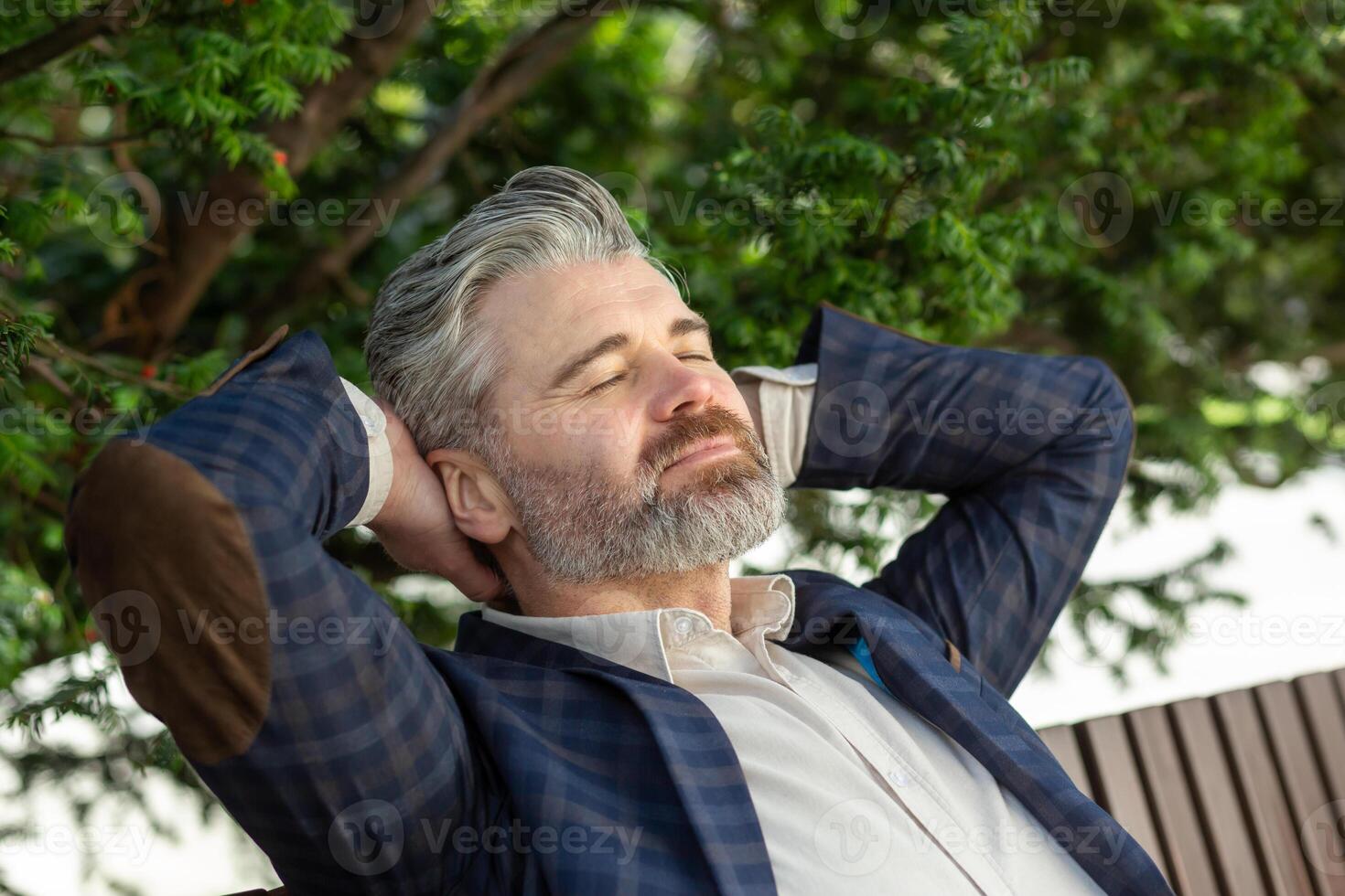 Senior professional man in business attire takes a peaceful break outdoors, reflecting with eyes closed amidst greenery. photo