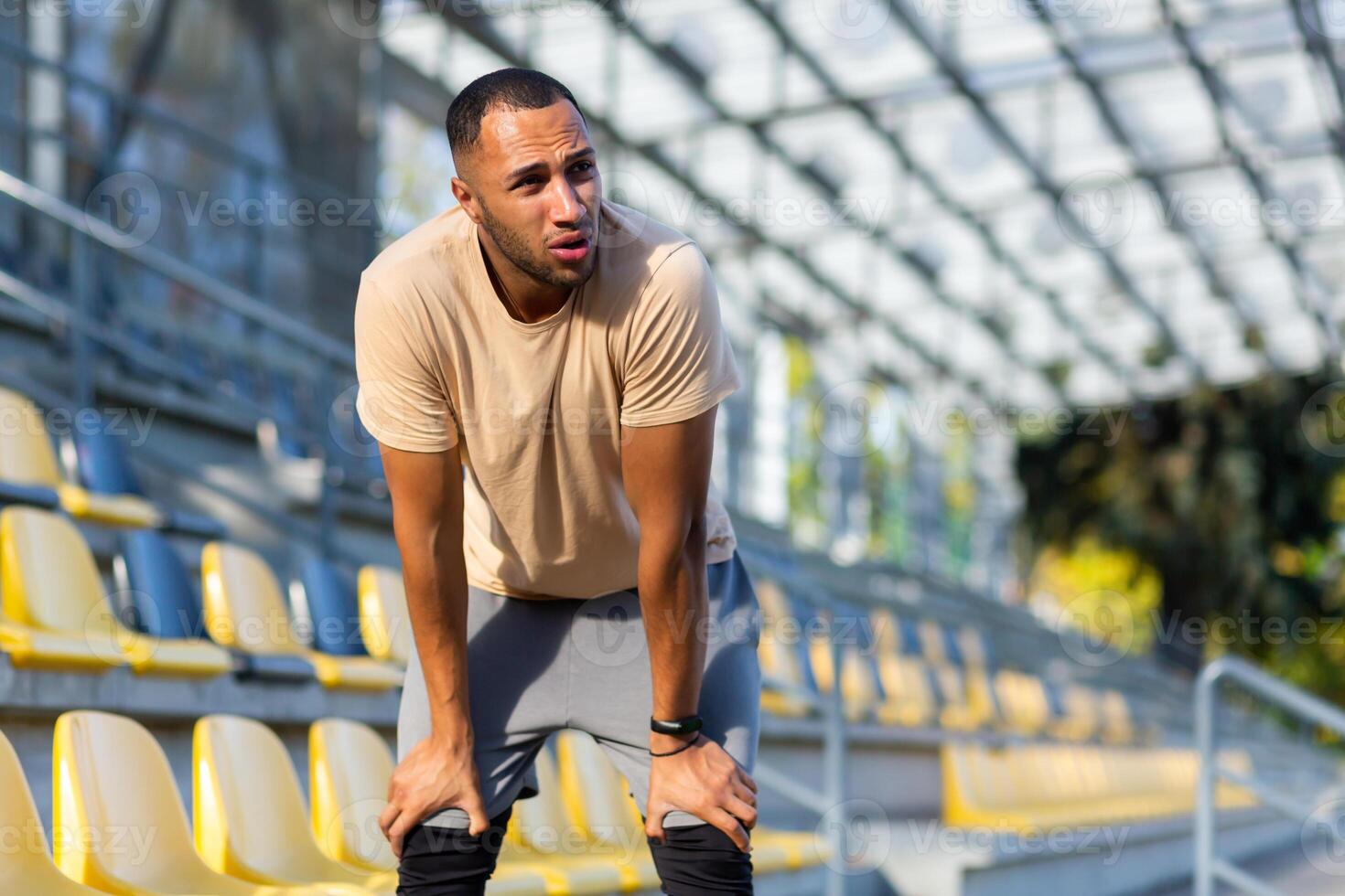 Tired hispanic athlete bent over and breathing after jogging, man doing sports on sunny day with active exercises and fitness, athlete resting after jogging. photo