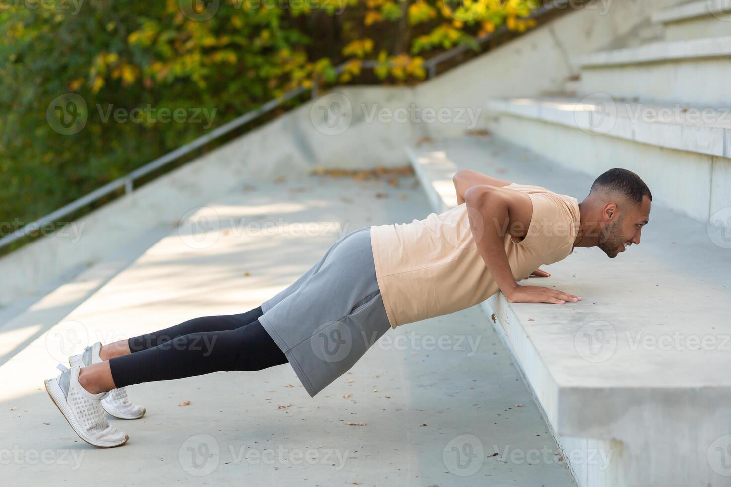 Cheerful and smiling hispanic man doing outdoor exercise in stadium, man stretching and recuperating before jogging in summer park. photo