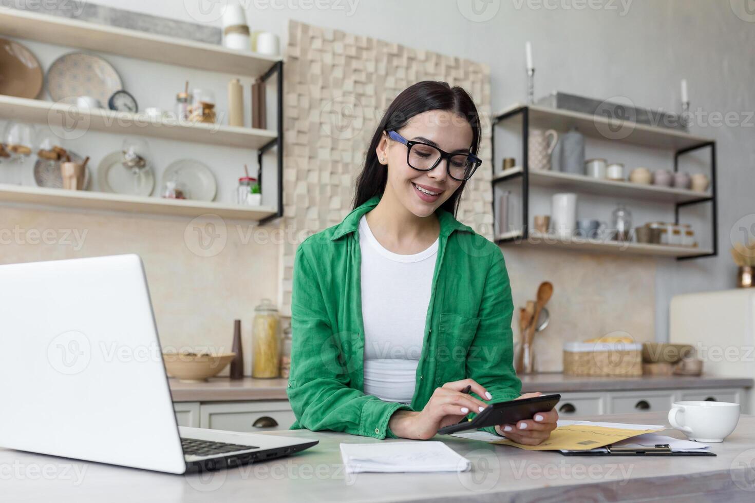 A young tired woman is sitting at the table in the kitchen at home. He works on a laptop and with documents, checks accounts, calculates the family budget. business income. photo