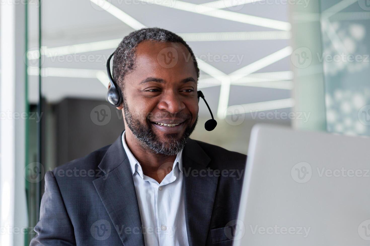 Mature experienced man in business suit with headset phone, working inside office with laptop, businessman online customer support worker, consulting customers remotely, selling in telestore. photo