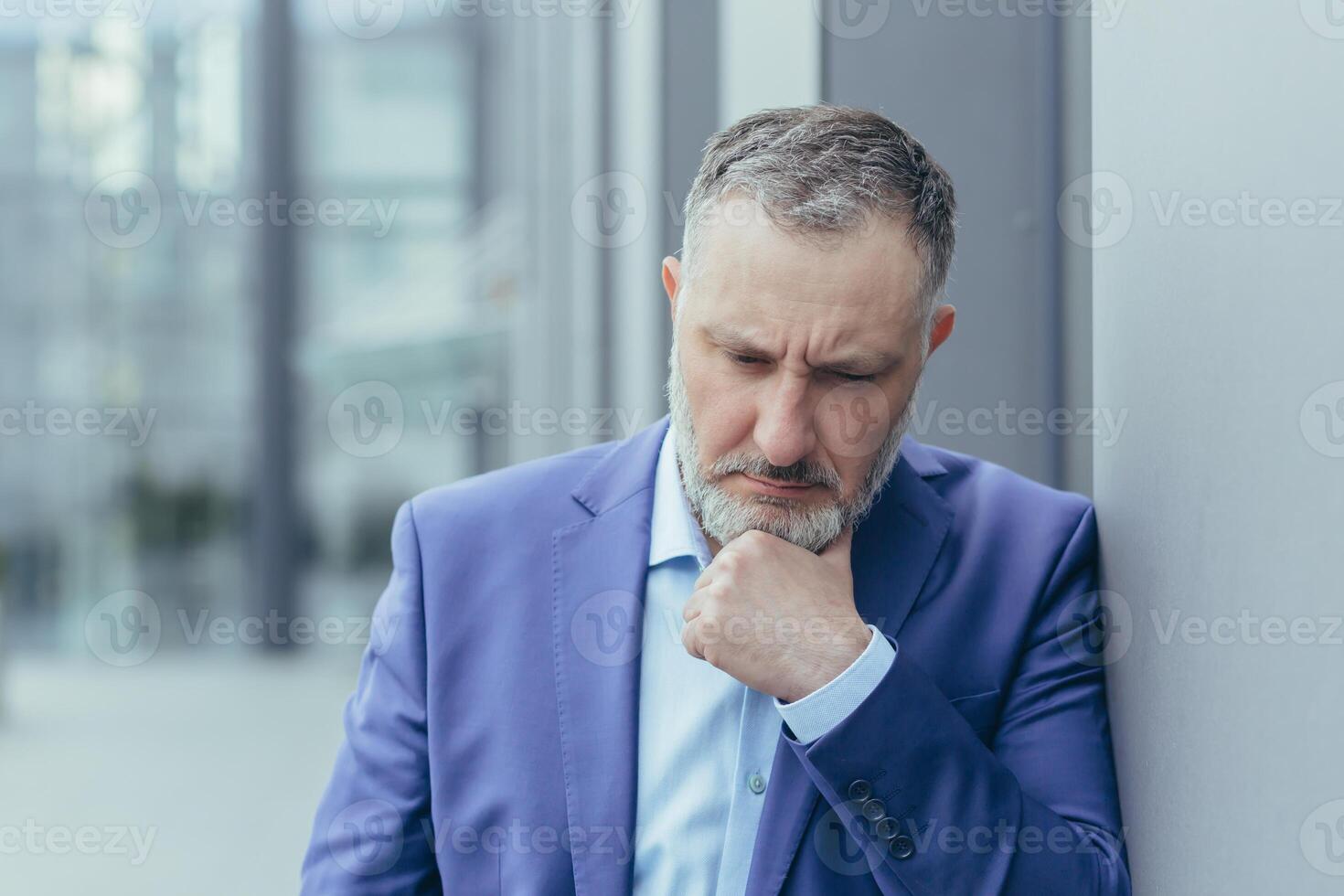 Senior gray haired man outside office building, standing and thinking, confused and sad businessman boss in business suit, over decision photo