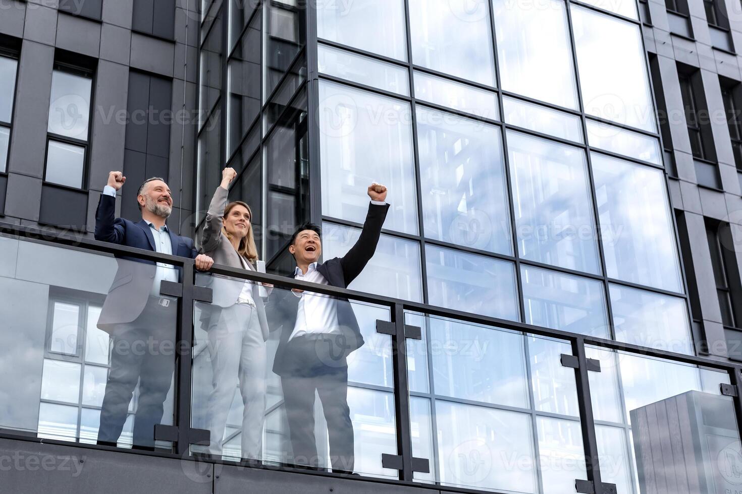 Diverse business group of people colleagues in business clothes outside office building, male and female employees rejoice and celebrate victory hold hand up and smile successful team photo