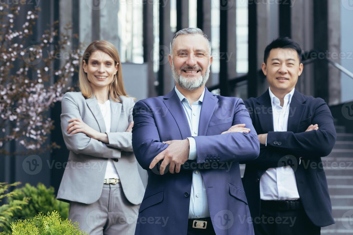 diverse dream team, senior gray haired businessman boss with colleagues outside office smiling and looking at camera with arms crossed photo