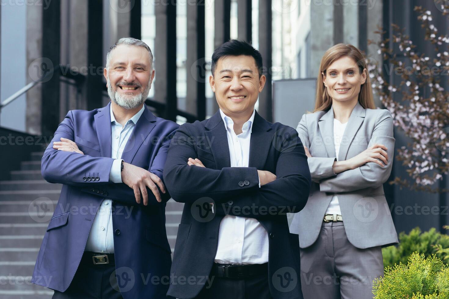 Portrait of successful and happy asian boss with his diverse dream team, business people outside office building standing with arms crossed and looking at camera photo