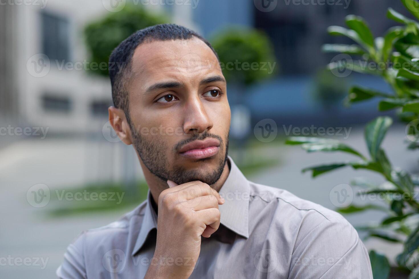 Pensive young African American man in shirt with a thoughtful expression walking near an office building or campus. photo